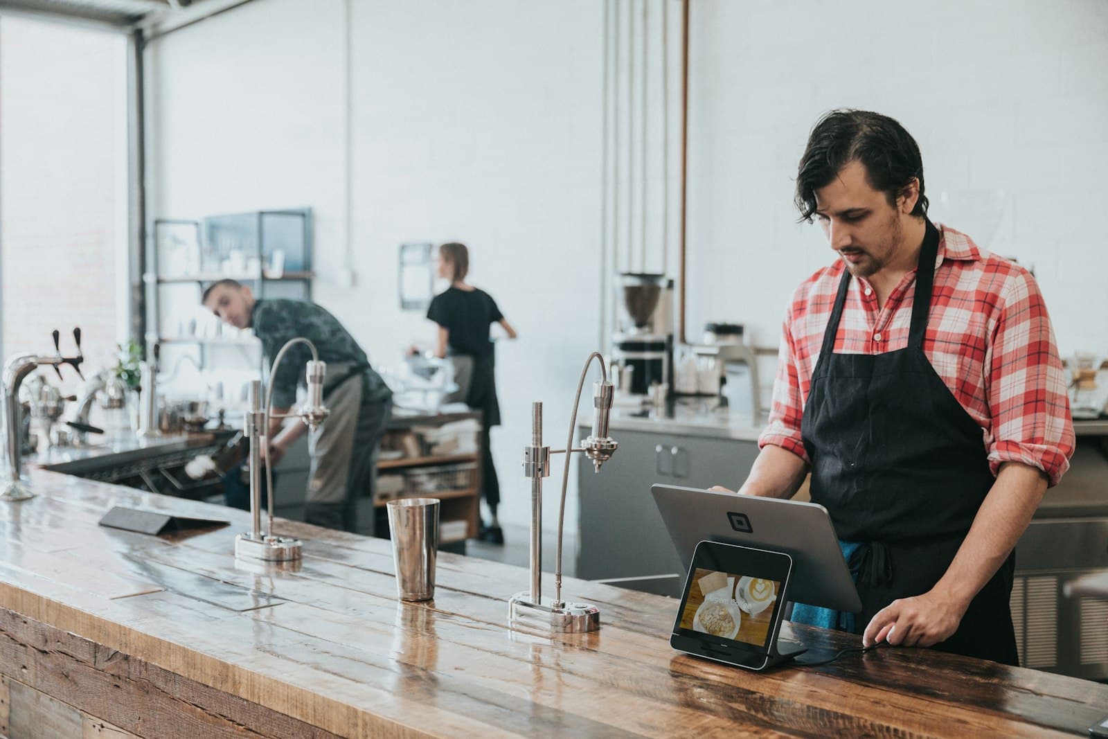 Barista in an apron using a tablet at a café counter